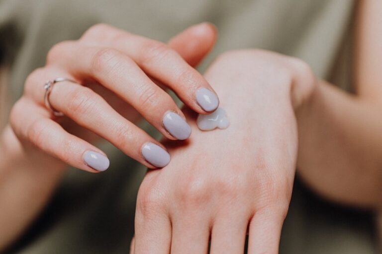 A woman's hand applying moisturizing cream, emphasizing skincare and nail beauty.